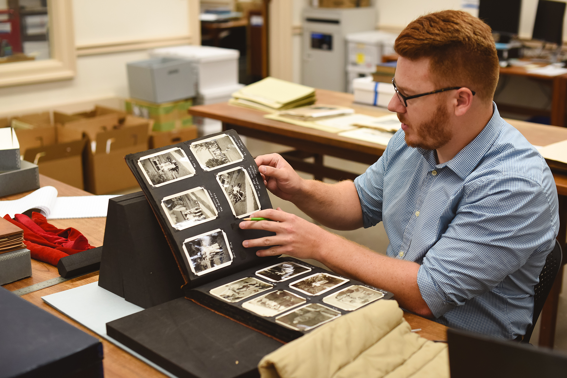 Student assistant sitting at a table turning the pages of a scrapbook that is being supported by black foam wedges.
