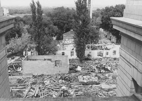 Black-and-white photograph of buildings in the process of being torn down; the ground around them is covered in rubble.
