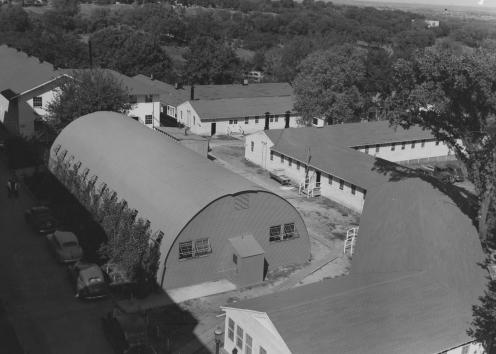 Black-and-white photograph of white wooden buildings built to surround a domed Quonset hut.